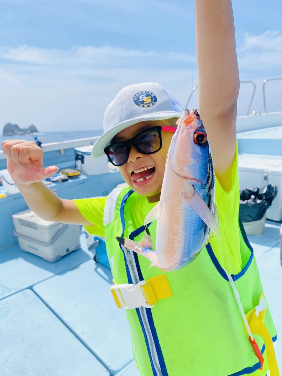 釣れた魚を高く掲げて喜ぶ葵葉くん。STANDING SOULのキャップを着用